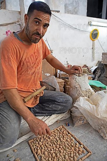 Moroccan cellular craftsman at work: hammering small pieces out of a tile