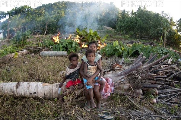 Family sitting on fallen tree near burning rubbish