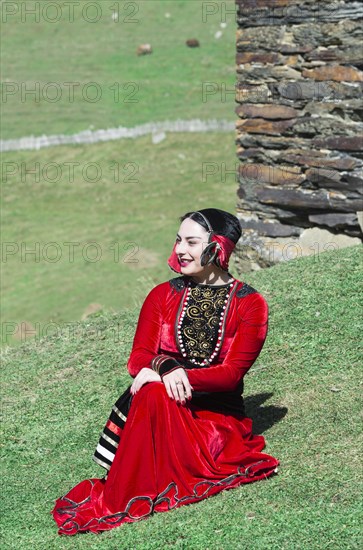 Georgian woman from a folkloric group sitting on the ground in front of a tower