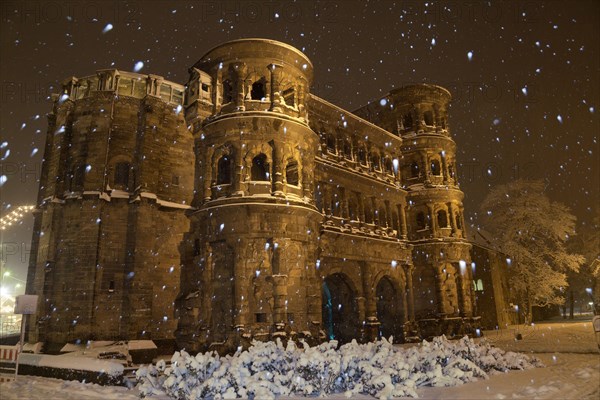 Roman city gate illuminated during snowfall at night