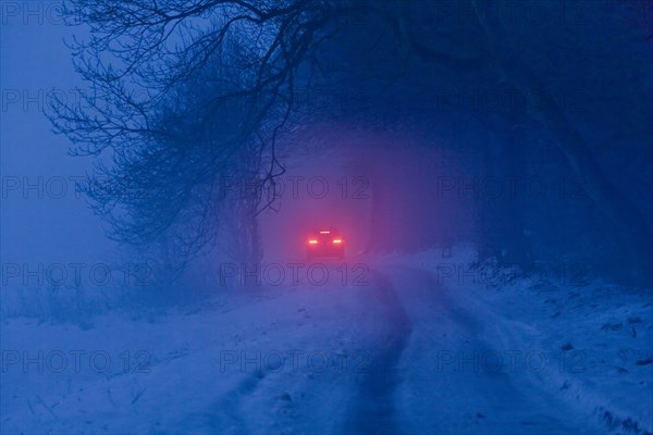 Distant brake lights of a car on a snow-covered road in freezing fog at dusk