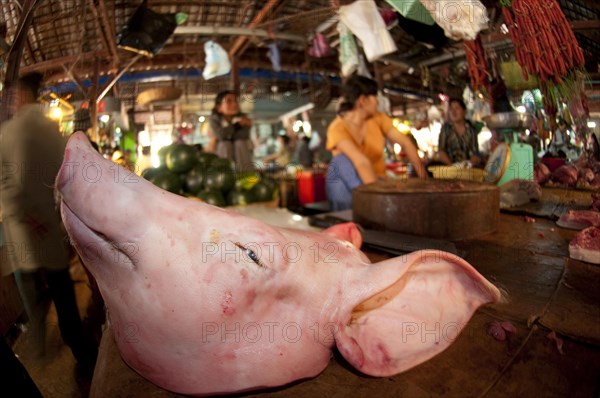 Butcher with pig's head for sale in a market hall