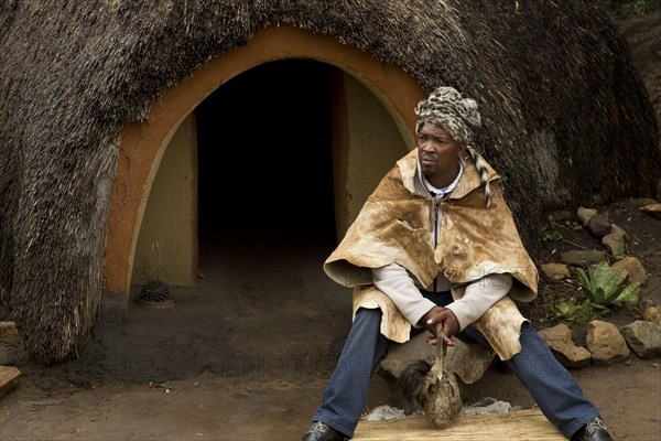 'Inyanga' herbal healer sitting outside hut in traditional Basutho village