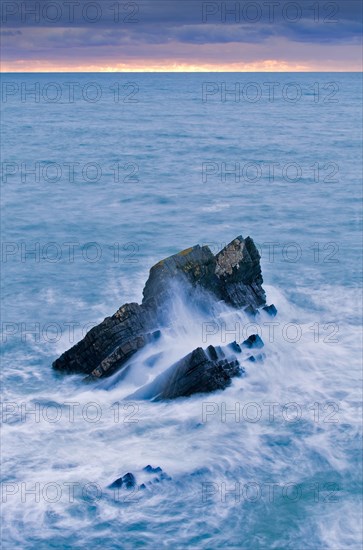 Large rock at sunset in stormy sea lashed by waves