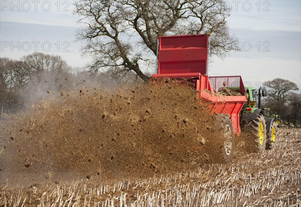 Tractor with manure spreader applying farmyard manure to maize stubble field
