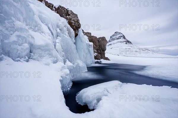 Kirkjufell mountain and the frozen waterfall Kirkjufellsfoss on Snaefellsnes peninsula in the snow in winter