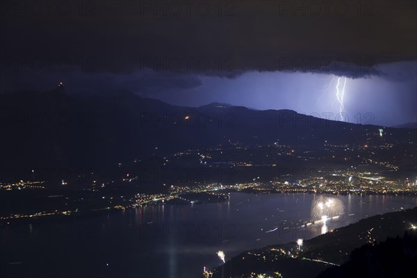 Thunderstorm with lightning and fireworks over town and lake at night