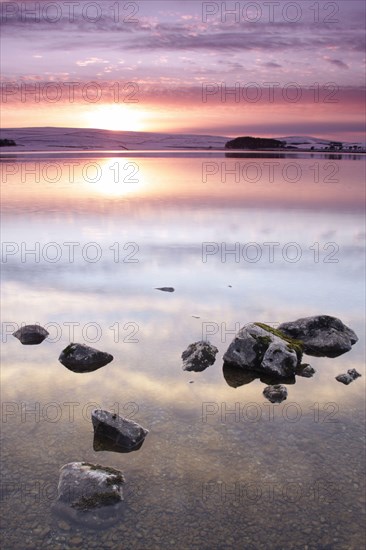 View of rocks in glacial lake at sunset after snowfall