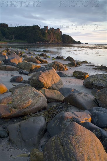 View of the rocks on the beach and the castle on the cliff at sunset