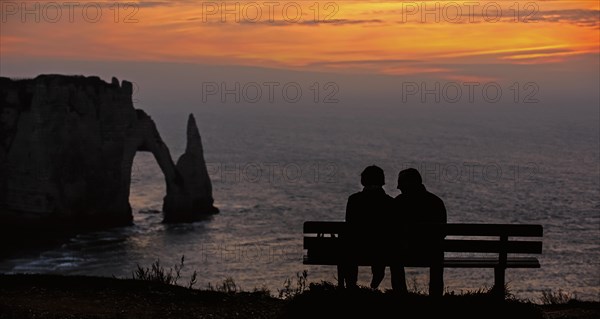 Elderly tourists sitting on a bench looking at the Porte D'Aval