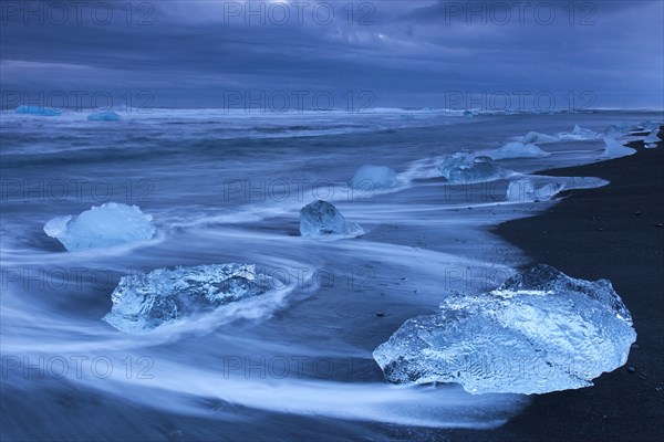 Melting ice blocks washing up on the beach along the Atlantic coast at Breidamerkursandur black sands in winter