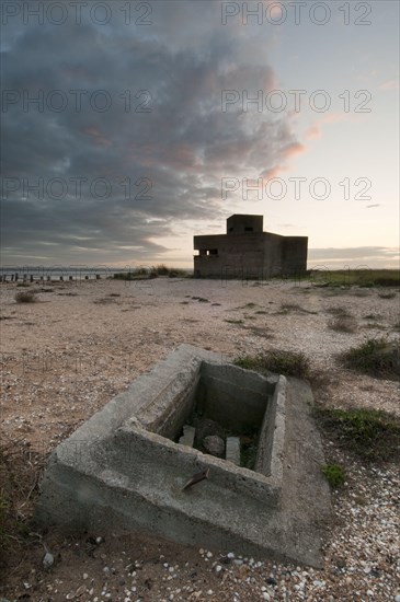 Remains of a World War II log cabin on a shingle beach at sunset