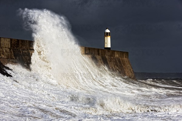 Coastal town seafront and lighthouse bombarded by waves in storm