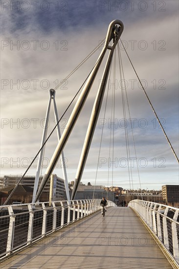 Man on bicycle crossing footbridge over river