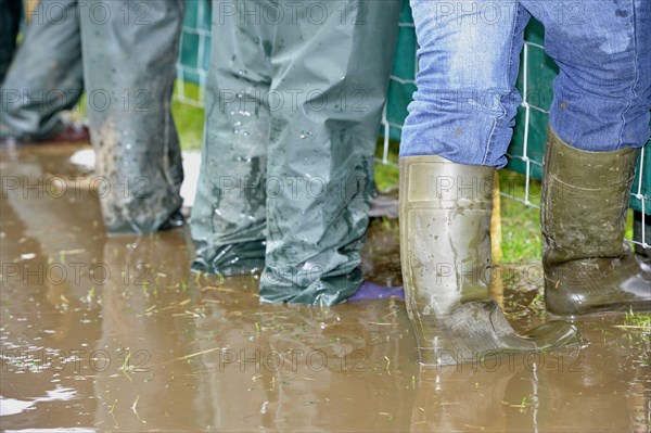 Farmers wearing wellington boots and waterproofs standing in puddle of muddy water