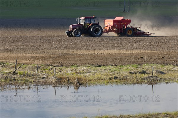 Case 5150 Tractor with Overum seeder sowing a field on the edge of a small river