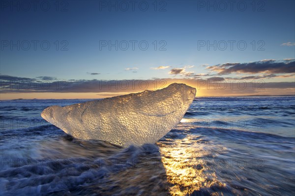 Melting ice block washing up on the beach along the Atlantic coast at Breidamerkursandur black sands in winter