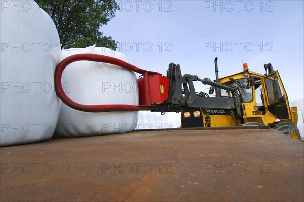 Plastic wrapped round silage bales stacked on trailer with mechanical loader