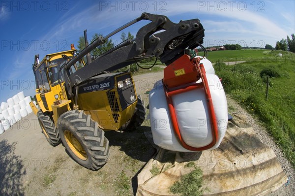 Plastic wrapped round silage bales stacked on a pile with mechanical loader