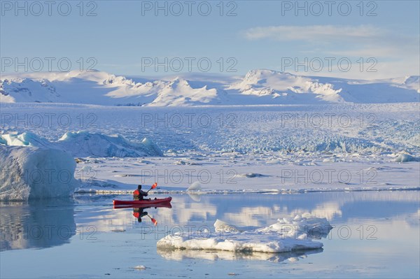 Kayaker in a red kayak on the glacier lagoon Joekulsarlon in winter