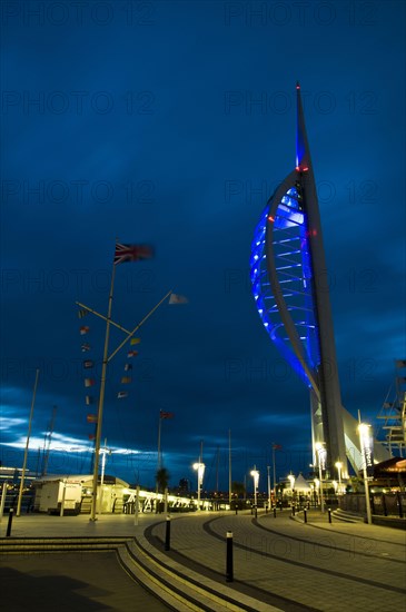 View of waterfront with Spinnaker Tower illuminated under stormclouds at dusk