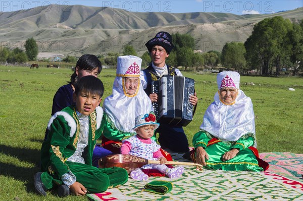 Kazakh family in traditional dress listening to the music of an accordion player