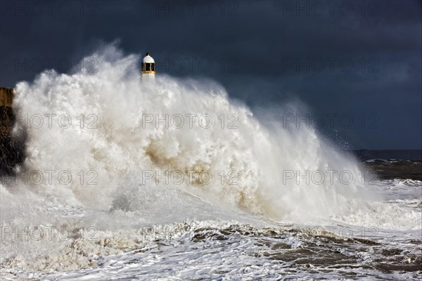 Coastal town seafront and lighthouse bombarded by waves in storm