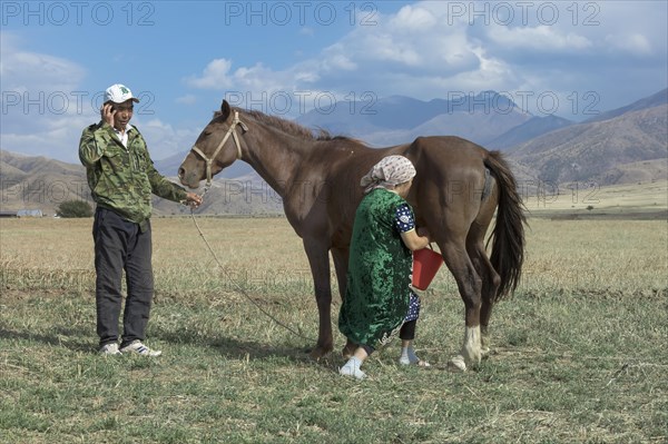Kazakh man with mobile phone and Kazakh woman milking a mare