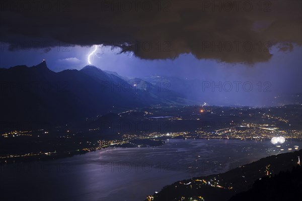 Thunderstorm with lightning and fireworks over town and lake at night