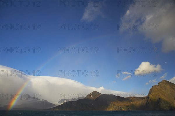 View of rainbow and moon over the coastline