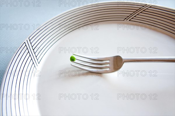 A fork with a single pea on an empty plate