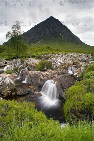 View of moorland with small waterfalls in rocky stream and mountain in background