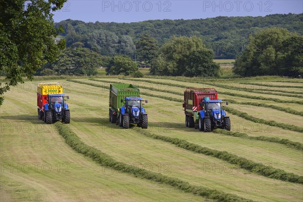 Three tractors with feed wagons picking up cut grass
