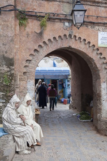 Men with djellaba sitting next to the medina arch in the city