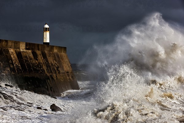 Coastal town seafront and lighthouse bombarded by waves in storm