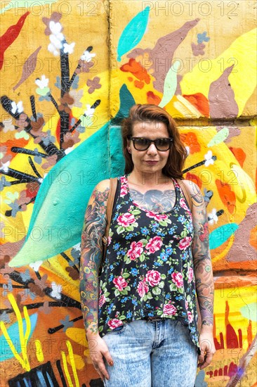 Tattooed woman in front of a wall covered with graffiti
