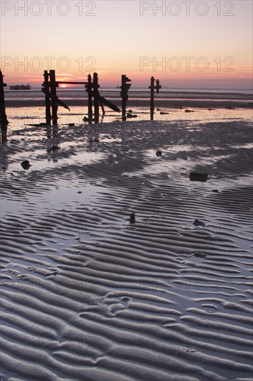 View of sand ripples and eroded groynes on the beach during low tide at sunset