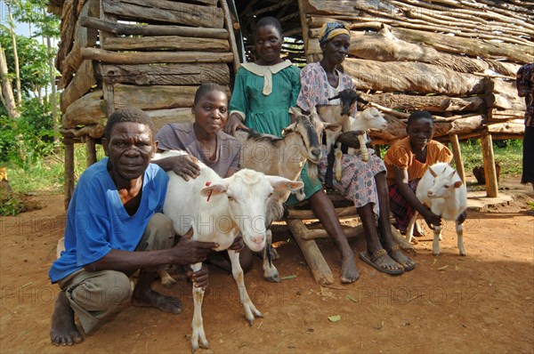 Family keeping domestic goats sitting in front of a wooden hut