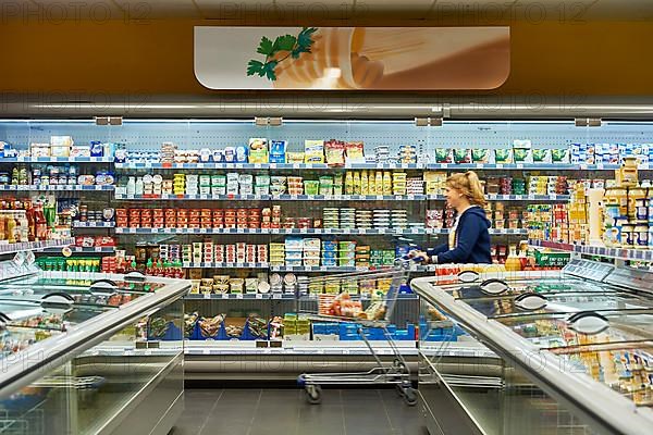 Woman pushing shopping trolley along a shelf