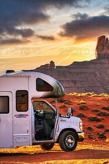 Motorhome with company logo parked on gravel road in front of striking rock formation