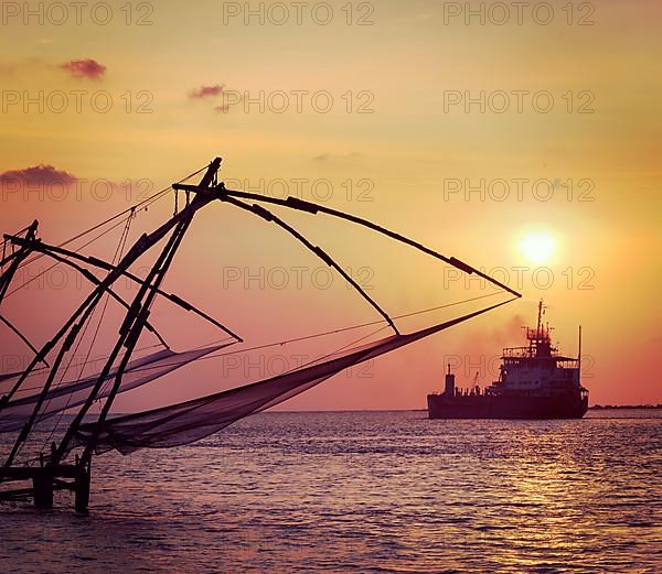 Vintage retro hipster style travel image of Kochi chinese fishnets on sunset and modern ship. Fort Kochin