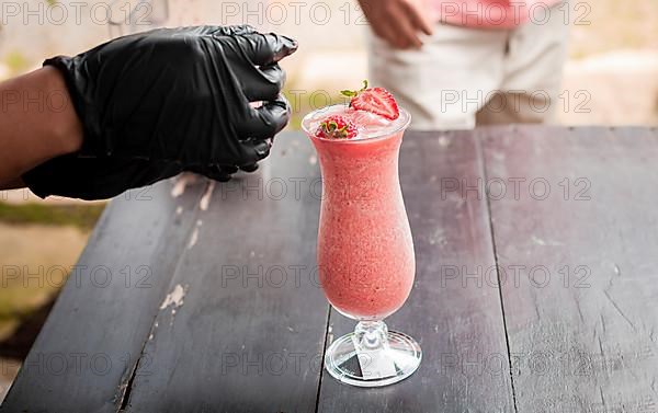 Hands decorating a strawberry smoothie on wooden table. Close up of hands making strawberry smoothie on wooden table. Close up of person decorating strawberry milkshake on table