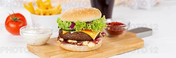 Hamburger cheeseburger fast food meal menu with fries and coke drink on wooden board Panorama in Stuttgart