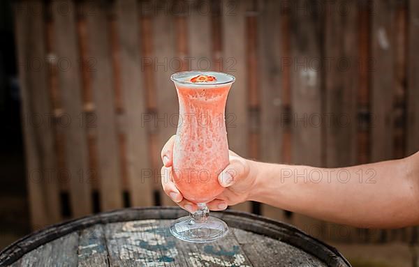 Hands holding strawberry smoothie on wooden table with blurred background. Hands showing strawberry smoothie on wooden table. People hand holding a strawberry milkshake on wood