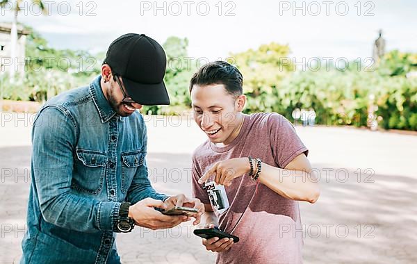 Two happy friends looking at a cell phone in the street