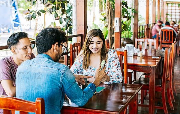 Three teenage friends on their cell phones in a coffee shop. Young friends in a coffee shop with their cell phones having a good time. Three people in a coffee shop with phones having a good time