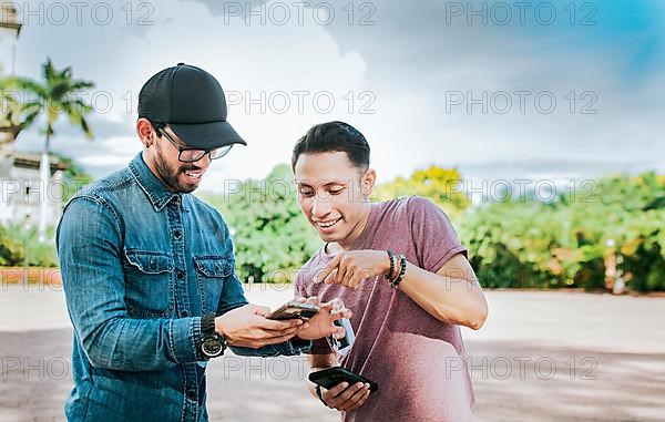 Two young friends having fun with the cell phone outdoors. Two happy friends looking at a cell phone in the street