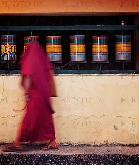 Vintage retro effect hipster style image of Buddhist monk with prayer beads passing and spinning prayer wheels on kora around Tsuglagkhang complex in McLeod Ganj