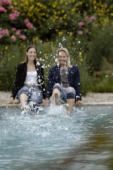 Couple sitting at the edge of the pool and splashing water