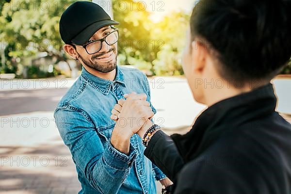 Concept of two friends greeting each other and shaking hands on the street. Two teenage friends shaking hands at each other outdoors. Two people shaking hands on the street